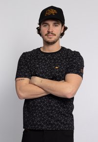 Zwarte korte mouwen t-shirt met een geometrisch patroon en een klein oranje berenlogo. Gekocht met een zwarte pet met een geometrisch berenontwerp.