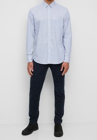Camicia a quadrati azzurri con maniche lunghe e taschino sul petto, abbinata a pantaloni blu navy e stivali alla caviglia neri.
