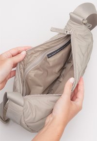 Beige quiltet håndtaske med en toplynlås, der har en glat indre foring og et mærke, der angiver, at den er lavet af genbrugsmaterialer.