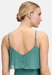 Haut en chiffon teal avec des bretelles fines réglables, présentant un design en couches et un dos plongeant. Texture lisse avec un drapé subtil.