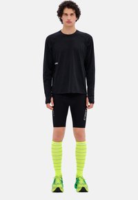 Maglietta nera a maniche lunghe, pantaloni corti neri attillati, calze a compressione gialle con strisce alte fino al ginocchio, e scarpe da corsa verdi. Loghi visibili sugli indumenti.