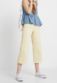 Ljusgula vida byxor med en cropped skärning, tillsammans med en blårandig peplumtop och vita sneakers. Enkelt, avslappnat stylande.