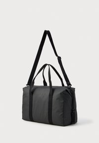 Μαύρη τσάντα duffel φτιαγμένη από λείο νάιλον, με διπλούς επάνω λαβές, αποσπώμενο ιμάντα ώμου και φερμουάρ για κλείσιμο.