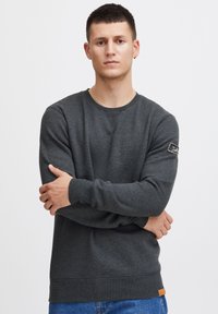 Donkergrijze sweatshirt met een ronde hals, geribbelde mouwen en een patch op de linkermouw. Gemaakt van gestructureerde stof en heeft een leren label aan de onderkant.