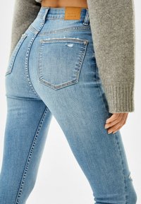 Jeans de tiro alto en azul claro con un acabado texturizado, que cuentan con bolsillos traseros y un ligero desgaste sutil. Parche de cuero de la marca en la cintura.