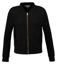 Musta vetoketjullinen takki, jossa on pystykaulus, kultainen vetoketju, pitkät hihat ja ribbineuleet hihansuissa sekä helmassa. Pehmeä kangas, jonka pinta on sileä.