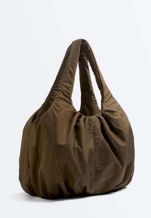 Zachte, oversized bruine handtas met gewatteerde, brede handvatten en een verzamelde, licht gerimpelde stoftextuur tegen een witte achtergrond.