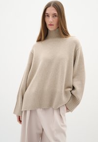 Krémový pletený svetr s rolákem, ribovaným lemem a manžetami, s uvolněným střihem a mírně oversized designem. Hladká textura.