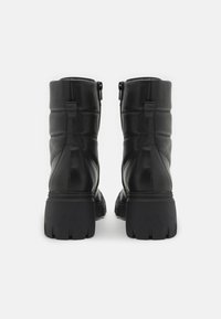 Botas de cuero negro hasta el tobillo con un diseño acolchado, que cuentan con punta redondeada, cremalleras laterales y una suela de goma gruesa con profundas bandas de rodadura.