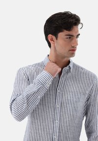 Camicia con bottoni, a righe verticali blu e bianche, maniche lunghe, colletto e taschino sul petto. Realizzata in un tessuto leggero.