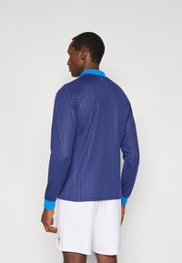 Camicia a maniche lunghe in navy con righe verticali, con colletto azzurro chiaro. Realizzata in tessuto leggero con una texture liscia.