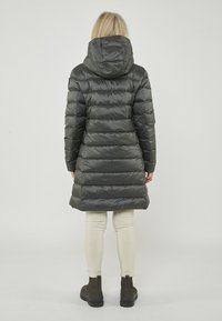 Grau gepufferter Mantel mit Kapuze, knielang, mit horizontalen Steppungen und glänzendem Finish, kombiniert mit cremefarbenen Leggings und dunklen Stiefeln.