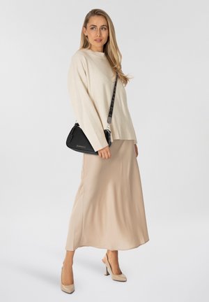 Pull en maille beige clair avec des épaules tombantes, associé à une longue jupe en satin beige fluide. Accessoirisé avec un sac à main noir.