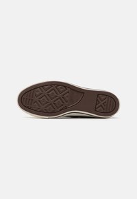 Pruuni kummist sneakerite tald geomeetriliste täkkepatternitega ja sissepressitud logoga. Välimine äär on kreemikas, sisaldades skulpturaalseid sektsioone haardeks.