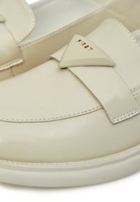 Mocassini beige realizzati in pelle liscia, caratterizzati da un accentuato triangolare con la scritta "FIRST" in rilievo dorato e un bordo cucito.