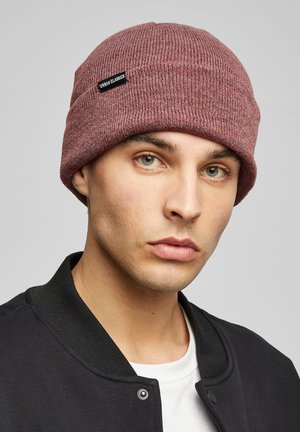 Pletená čiapka v burgundskej farbe s textúrovaným rebrovaným dizajnom. Obsahuje čierny štítok s nápisom "URBAN CLASSICS." Nosí ju model v čiernej bunde.
