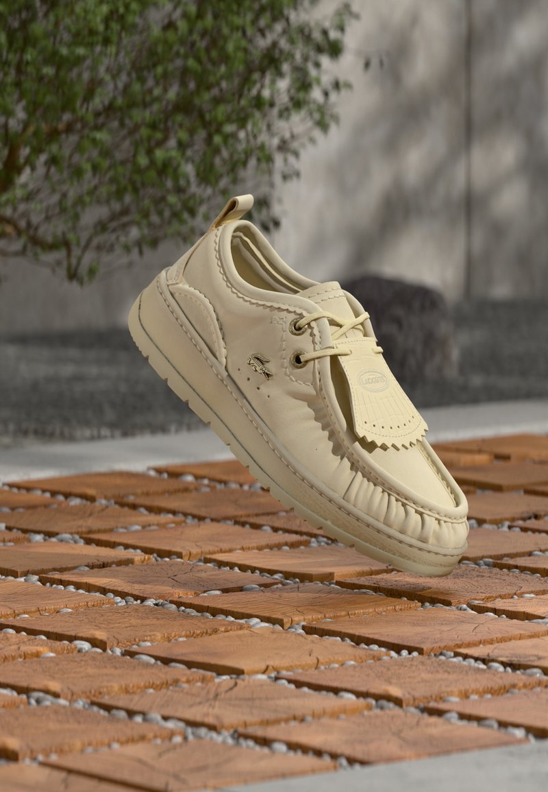 Chaussure bateau en cuir beige clair avec couture décorative, fermeture à lacets et semelle en caoutchouc. Comprend une étiquette de marque et une finition douce et texturée.