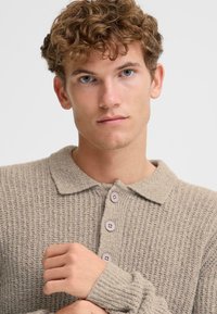 Light beige knit sweater with a collared neckline, featuring four button fastenings, ribbed cuffs, and a textured pattern.