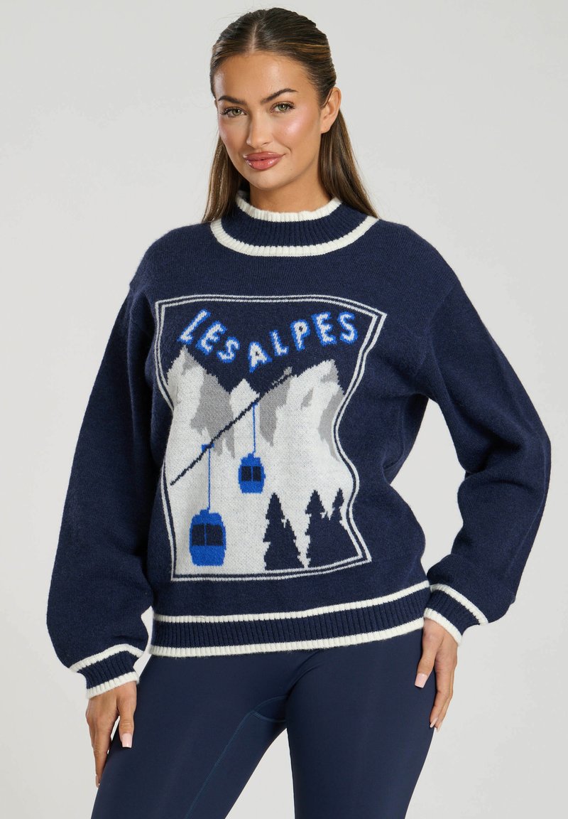 Maglione a maglia blu navale con un grafico di montagne, funivie e "LES ALPES" in blu, con rifiniture bianche al colletto e ai polsini.