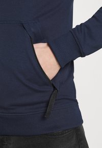 Marinblå sweatshirt med en dragkedjeficka på sidan, ribbad mudd och en slät, mjuk textur.