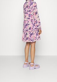 Květinové šaty v purpurové, růžové a krémové barvě, s dlouhými rukávy, nařaseným pasem a volánkovým lemem. Kombinované s fialovými robustními sandály.