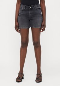Shorts de mezclilla gris oscuro con cintura alta, cinco bolsillos y dobladillo remangado, combinados con sandalias negras de tiras. Textura suave.