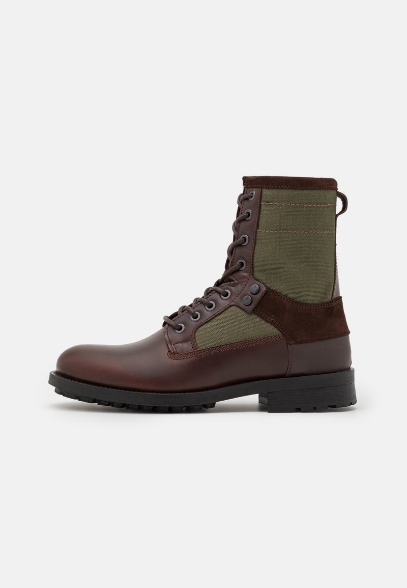 Botte en cuir marron et toile vert olive avec un devant à lacets, un talon renforcé et une semelle en caoutchouc texturée. Détails de couture élégants inclus.