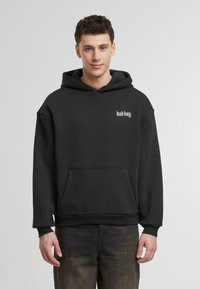 Felpa con cappuccio nera realizzata in morbido tessuto, dotata di tasca frontale e testo bianco "bad boy" sul lato sinistro del petto.