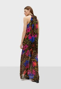 Vestido maxi de tela transparente con un audaz patrón floral en rosa, azul y verde sobre un fondo de estampado de leopardo. Se ata en la parte posterior.