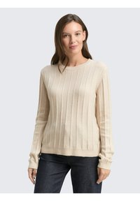 Beige Rippenstrickpullover mit langen Ärmeln und Rundhalsausschnitt. Weiche Textur mit lockerer Passform. Kombiniert mit dunklen Jeans.