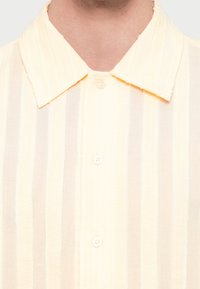 Ανοιχτό κίτρινο πουκάμισο με κάθετο ριγέ μοτίβο. Διαθέτει κλασικό γιακά και λευκά κουμπιά. Μαλακή υφή.