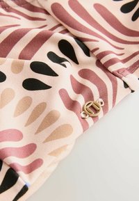Haut en tissu rose clair avec des motifs abstraits en noir et en nuances de rose, comportant un petit détail en métal doré sur l'ourlet.