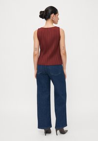 Haut sans manches côtelé bordeaux associé à un jean en denim foncé à jambes larges. Le haut présente une finition texturée ; le jean a de subtils détails de couture.