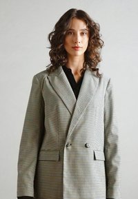 Sacou gri cu carouri, cu un design cu două rânduri de nasturi, rever bine definit și două buzunare frontale; material texturat cu linii verticale și orizontale.