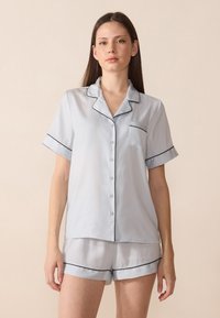 Ensemble de pyjama en soie bleu clair comprenant un haut à manches courtes avec boutons, une poche et des bordures noires, associé à un short assorti.