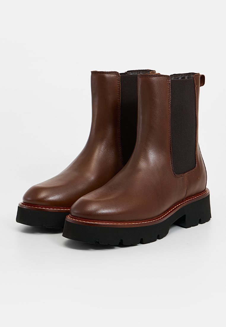 Braune Leder-Ankle-Boots mit elastischen Seiteneinsätzen, einer groben schwarzen Sohle und kontrastierender Naht entlang der Kante. Glatte Textur.