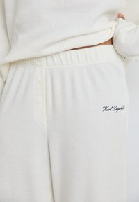 Conjunto de roupa de estar em malha waffle branca, apresentando uma blusa de corte descontraído e calças com placket de botões, cintura elástica e logótipo bordado.