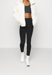 Vit fluffig jacka, svart crop top, svarta leggings och vita sportskor. Slät textur, avslappnad passform och kontrasterande färgpalett.