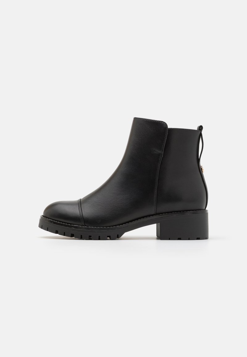Bottine en cuir noir avec un bout arrondi, un talon plat empilé et un subtil détail de couture. Comprend une languette à l'arrière.
