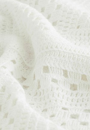 Textureret hvid hæklet tæppe med et åbent vævemønster og hævede detaljer, der fremviser et blødt og hyggeligt udseende.