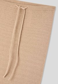 Tessuto a maglia beige con un motivo testurizzato, dotato di un cordoncino all'orlo superiore per una vestibilità regolabile.