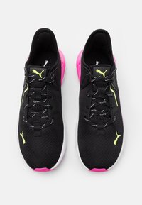 Schwarze Sportschuhe mit einem strukturierten Obermaterial, pinker Sohle und gelben Akzenten. Verfügt über Schnürsenkel und ein Logo auf der Zunge.