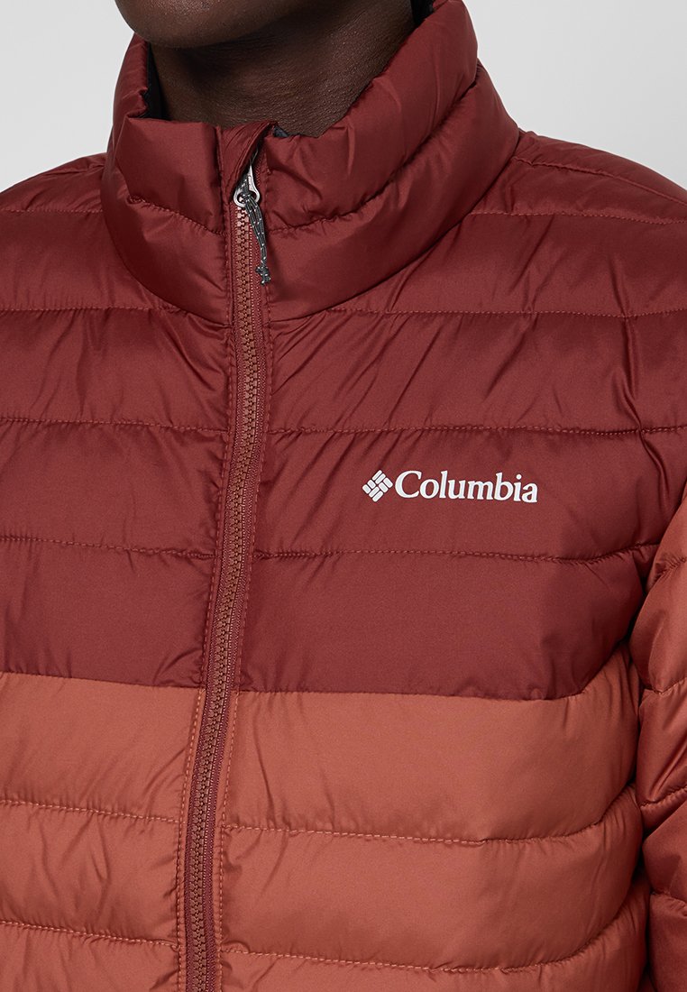 Chaqueta acolchada burdeos con cierre de cremallera, que cuenta con un cuello alto y un diseño de acolchado horizontal. Logo de Columbia mostrado en el pecho.