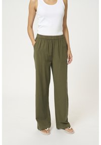Pantalons larges en vert olive fabriqués dans un tissu léger, avec une taille élastique et des poches latérales, associés à un débardeur blanc.