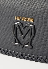 Borsa a mano in pelle sintetica nera con un logo in rilievo prominente e dettagli in oro e nero, rifinita con bordi intrecciati.
