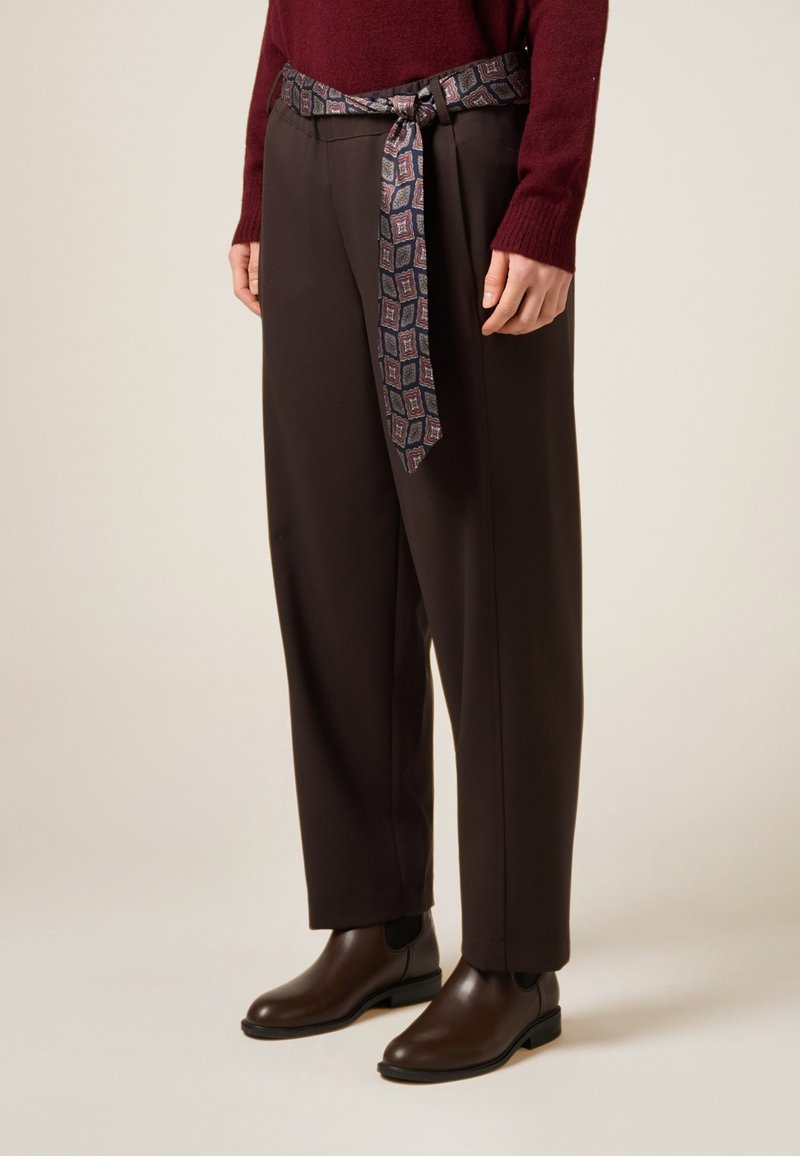 Brązowe spodnie o luźnym kroju, zestawione z pasem z wzorzystej tkaniny. Całość uzupełniają ciemnobrązowe skórzane buty typu Chelsea.