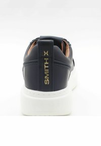 Sneaker in pelle blu navy con suola bianca, dotato di un logo dorato sul tallone e colletto imbottito per il comfort. Texture liscia con dettagli di cucitura.