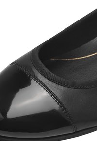 Zapato plano de cuero negro con una puntera brillante, textura suave, ribete elástico en la apertura y un sutil acento dorado en la plantilla.