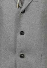 Giacca in lana grigia con un design sartoriale, sei bottoni e una tasca sul petto. Include una finitura strutturata e accessori in contrasto.