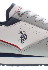 Zapatilla gris claro con una parte superior de cuero blanco, detalles en azul marino y rojo, un diseño texturizado y una impresión de jugadores de polo a caballo.